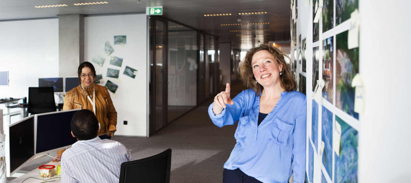 Vrouw geeft toelichting op foto's die aan de wand hangen