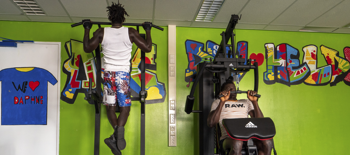 Twee bewoners op fitnessapparatuur voor een fel groene muur met grafitti