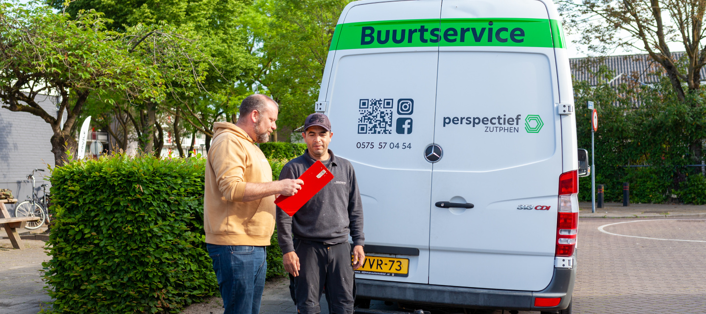 Man met gele hoodie geeft instructie aan man met zwarte pet bij het witte Mercedesbusje van de Buurtservice.