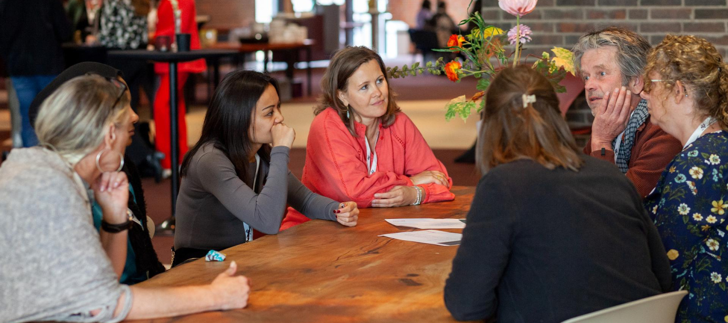 Verschillende casemanagers zitten aan tafel en zijn met elkaar in gesprek