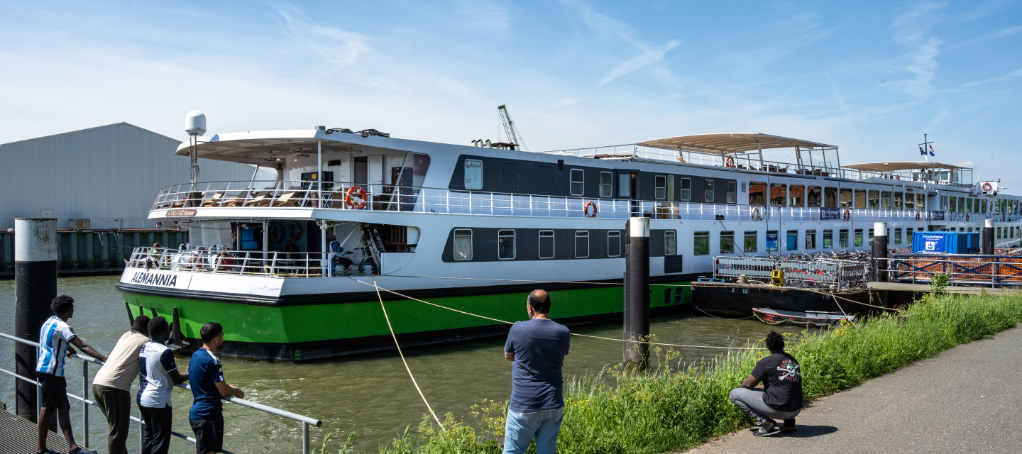 Asielzoekers kijken vanaf de kade naar het schip waar zij op wonen.