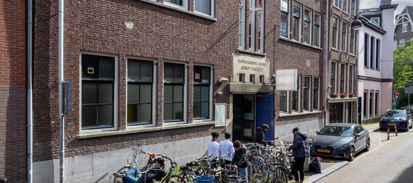 Straat met oud gebouw met fietsen ervoor en 5 jongens die hun fiets pakken