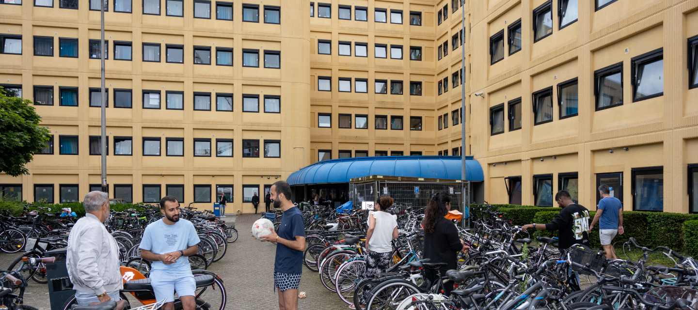 Statushouders staan voor de ingang van de noodopvang tussen heel veel fietsen.