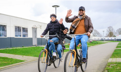 Twee zwaaiende mannen op de fiets op het terrein van he azc.