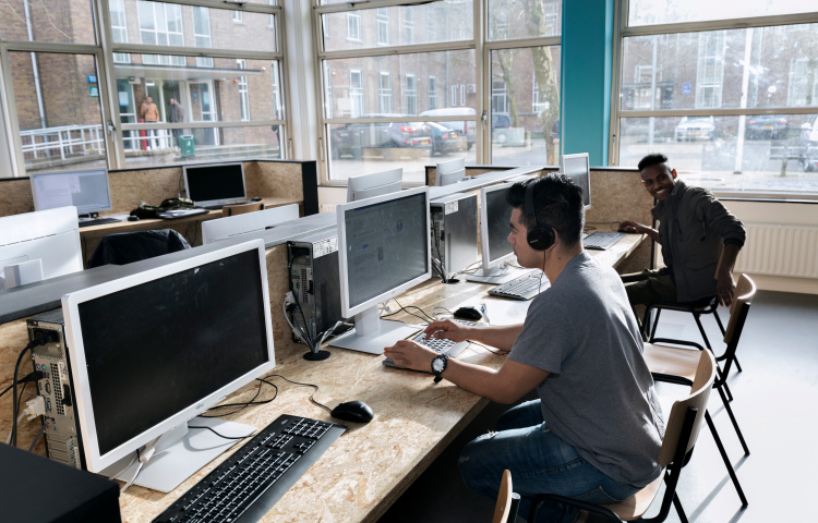 Asielzoekers werken achter computer in open leercentrum van azc