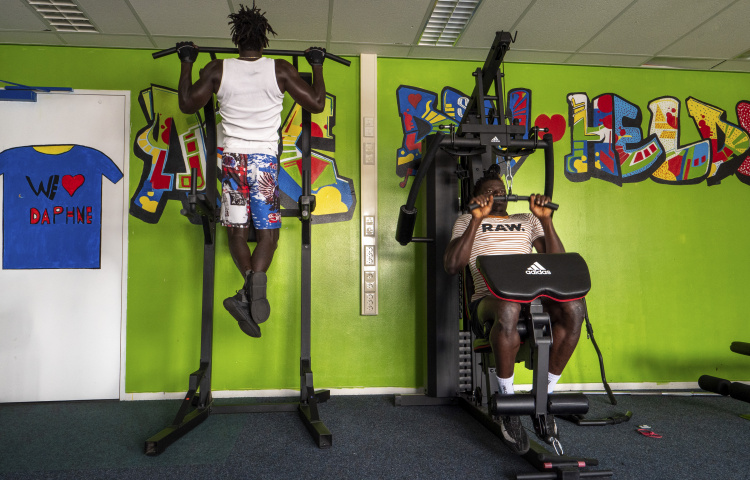 Twee bewoners op fitnessapparatuur voor een fel groene muur met grafitti