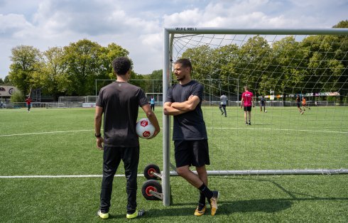 Keeper leunt tegen doelpaal en trainer heeft bal onder zijn arm
