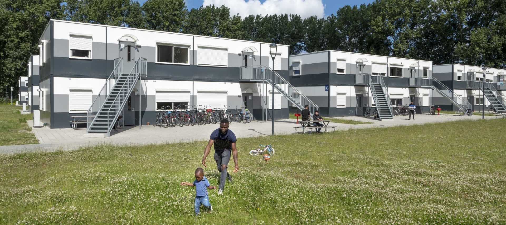Vader en kind in he gras voor woonblok azc