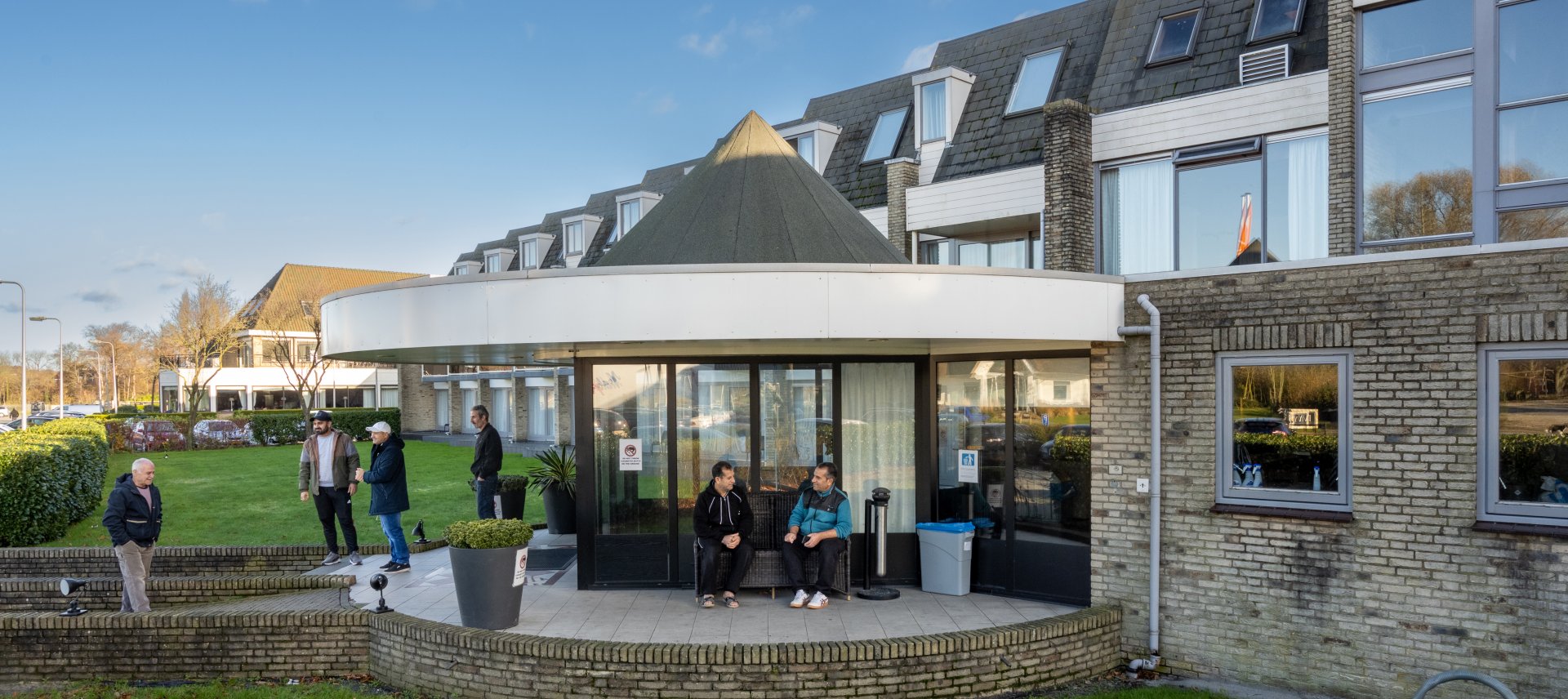 Mannen zitten voor de ingang van het hotel waar zij opgevangen worden.