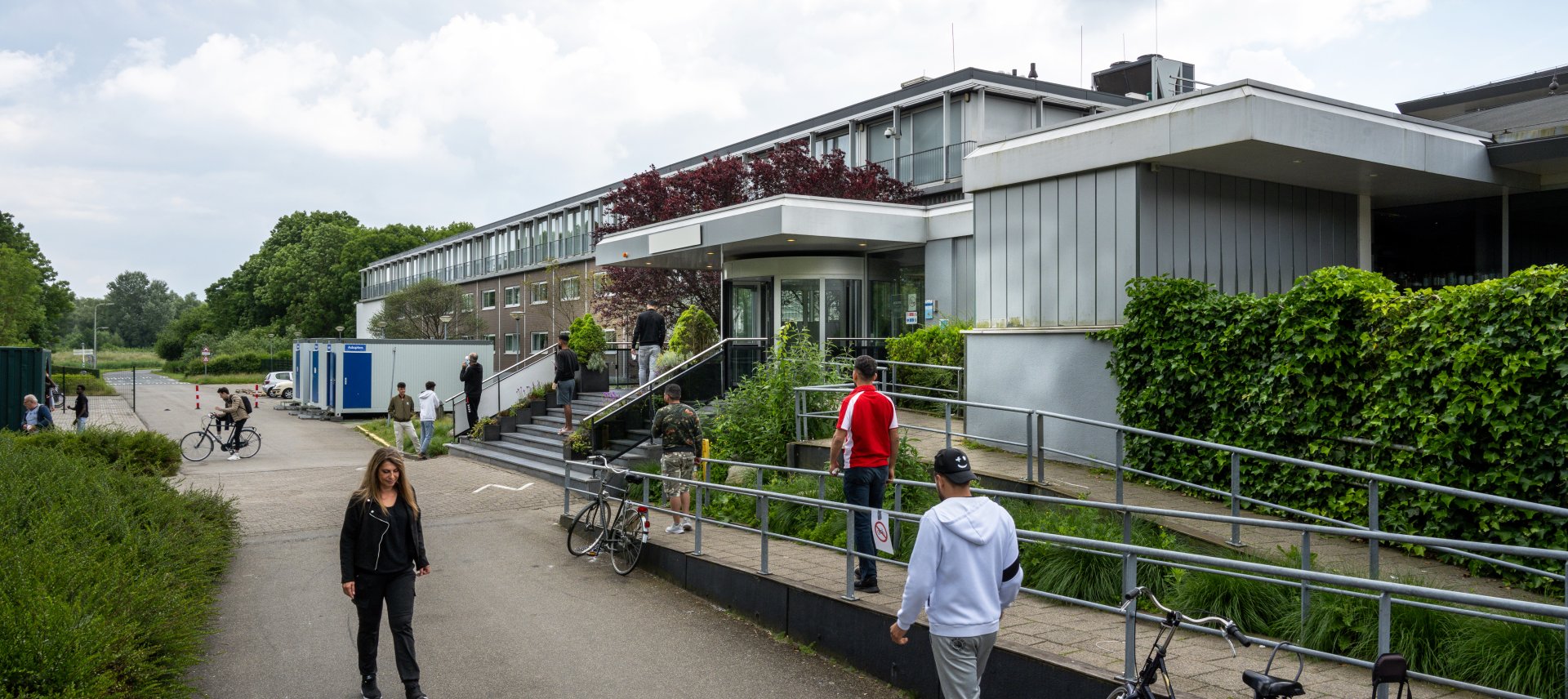 Medewerker en asielzoekers lopen voor de ingang van het gebouw.