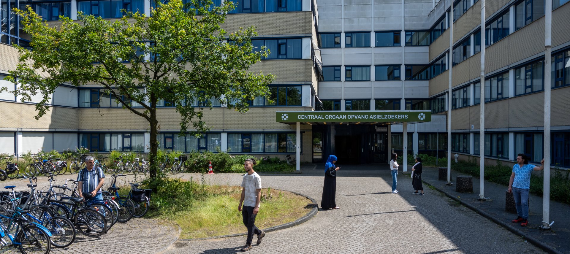 Coa noodopvang in een oud ziekenhuisgebouw, er staan mensen en fietsen voor de ingang