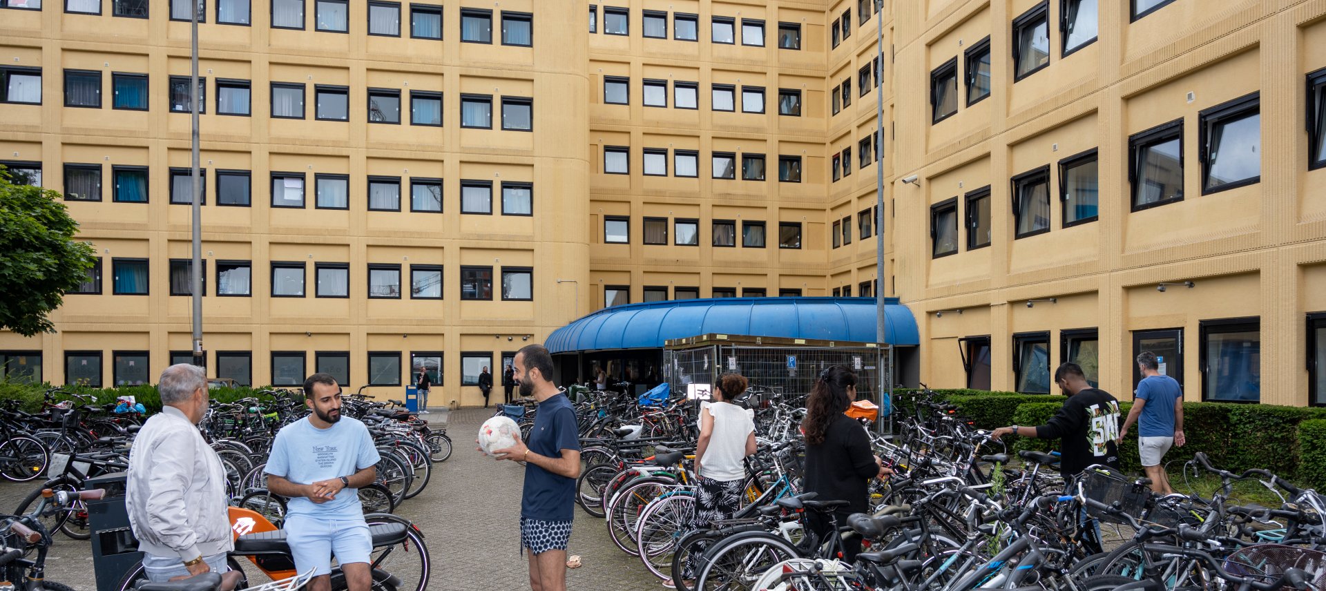 Statushouders staan voor de ingang van de noodopvang tussen heel veel fietsen.