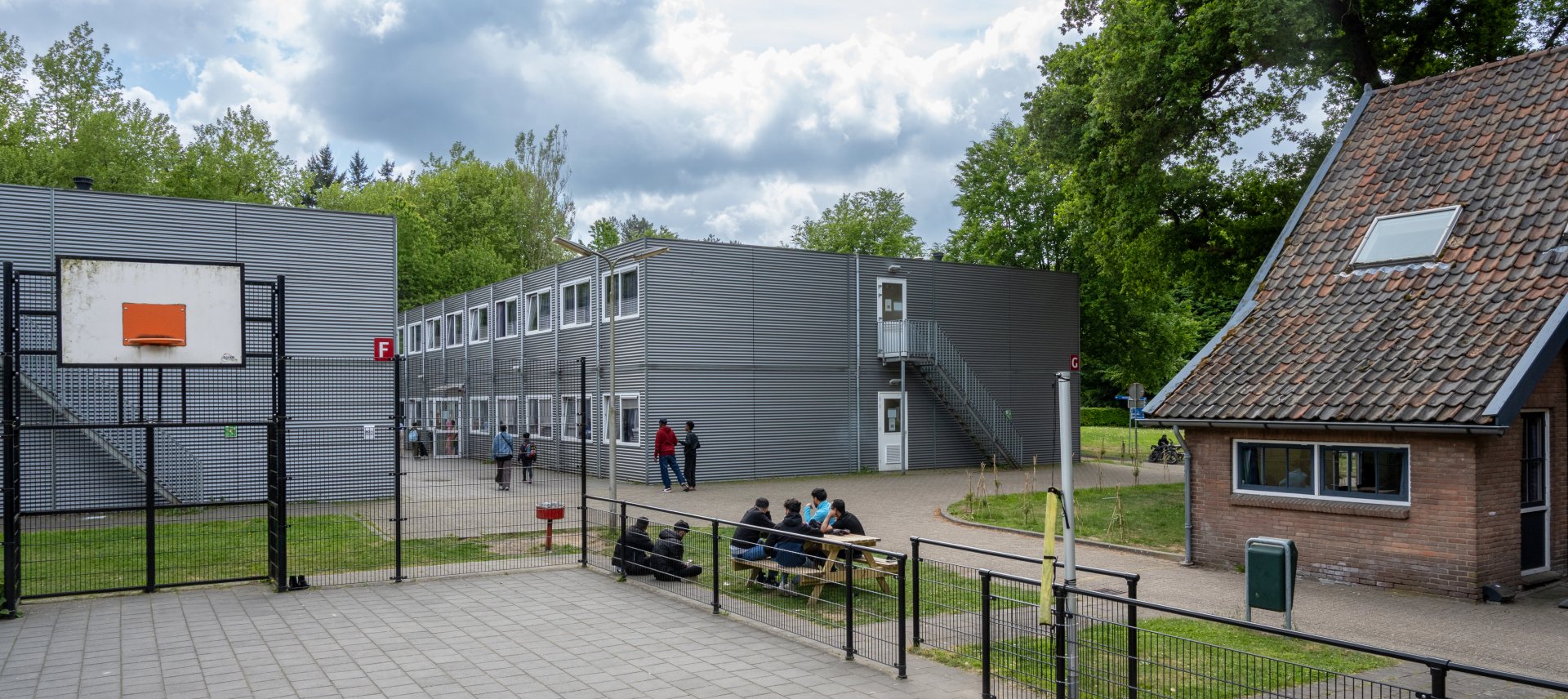 gebouw coa-locatie wageningen bosrandweg, 6 jongeren zitten bij het basketballveld aan de picknicktafel