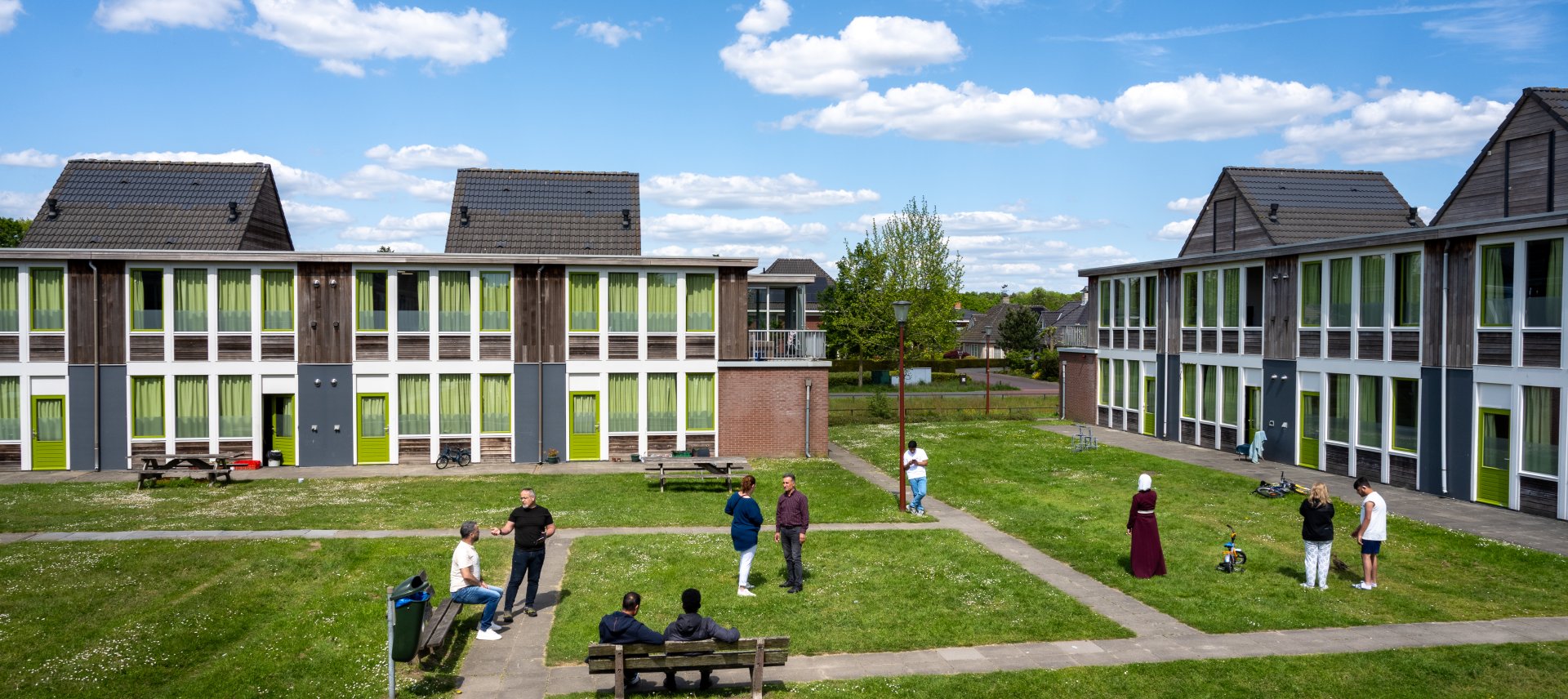gebouwen op coa locatie winterswijk amstelstraat, veel bewoners zijn buiten op het grasveld en de paden