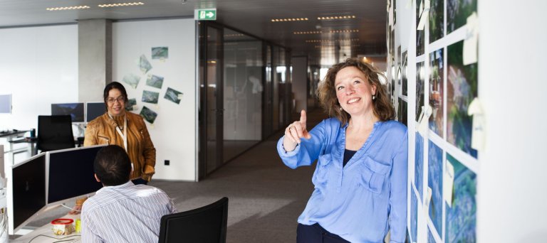 Vrouw geeft toelichting op foto's die aan de wand hangen