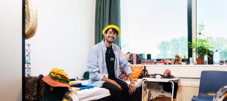 Jongeman met gele hoed zit op zijn bed in azc Leiden