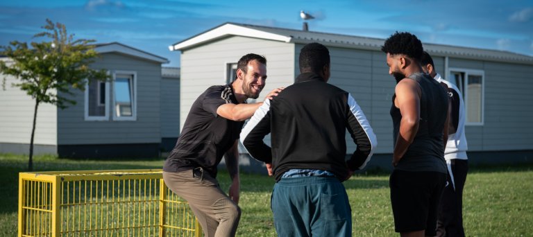 drie mannen met een voetbal en huizen op de achtergrond