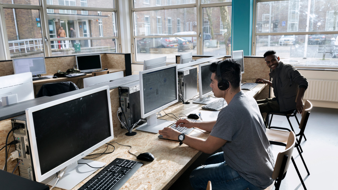 Asielzoekers werken achter computer in open leercentrum van azc