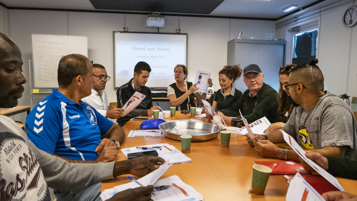 Bewoners aan een tafel die les krijgen in Basaal Nederlands