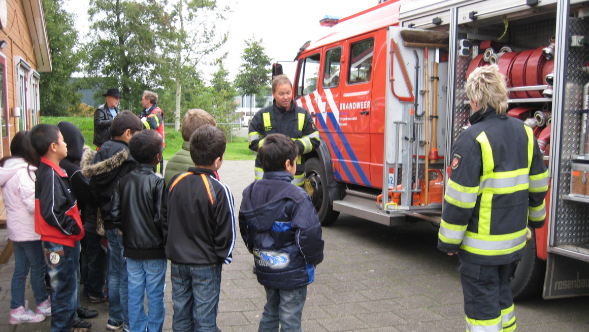 Kinderen in het azc staan bij een brandweerauto en krijgen voorlichting