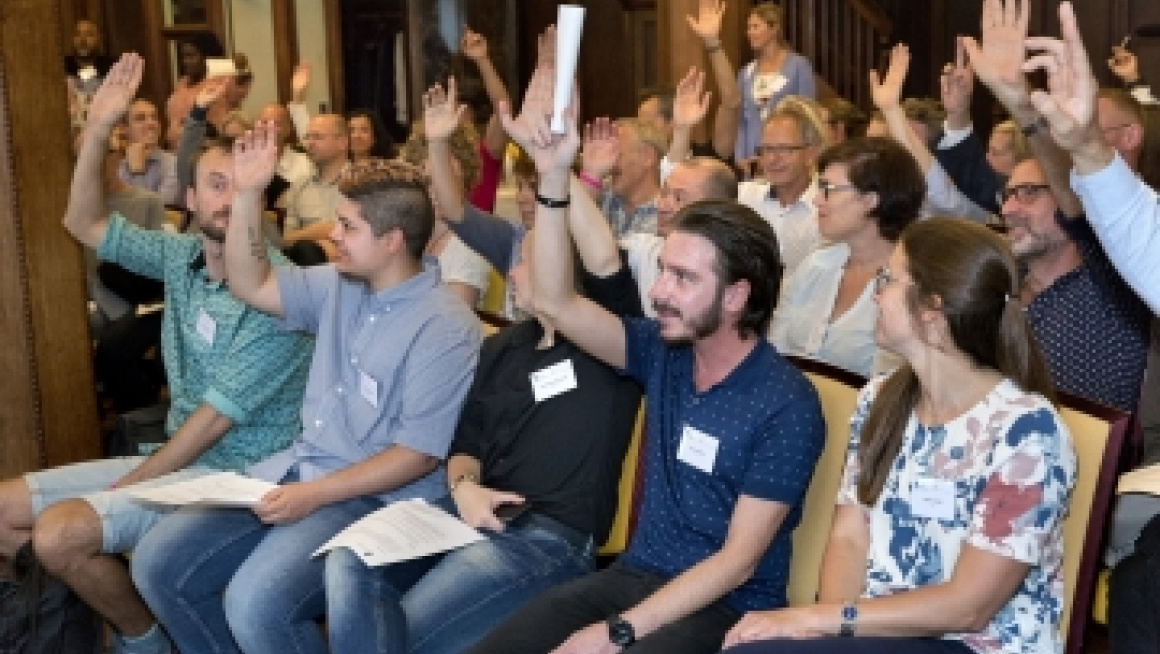 groepje zittende mensen steken hun handen op