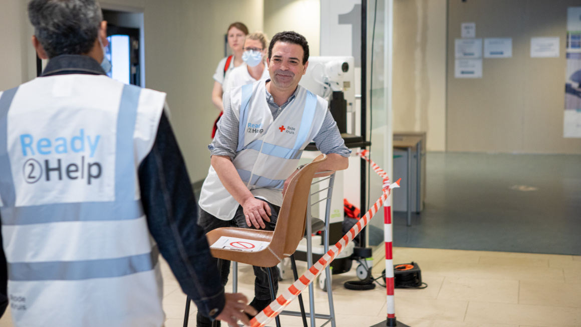 Twee bewoners van het COA staan op de gang met op de achtergrond twee verpleegkundigen. De bewoners assisteren in het Ikaziaziekenhuis