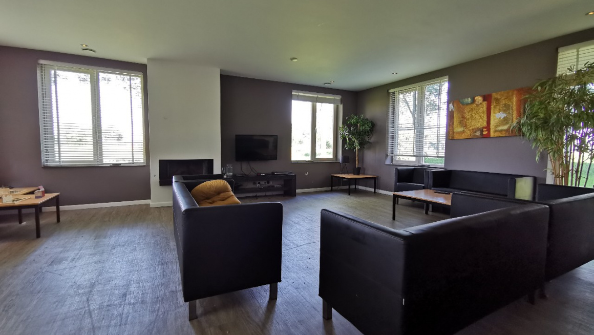 woonkamer met zwarte banken een salontafel, tv, houten vloer en mauve kleurige muren