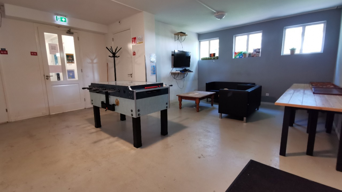 recreatieruimte met voetbaltafel een salontafel en zwarte banken, tv en kapstok