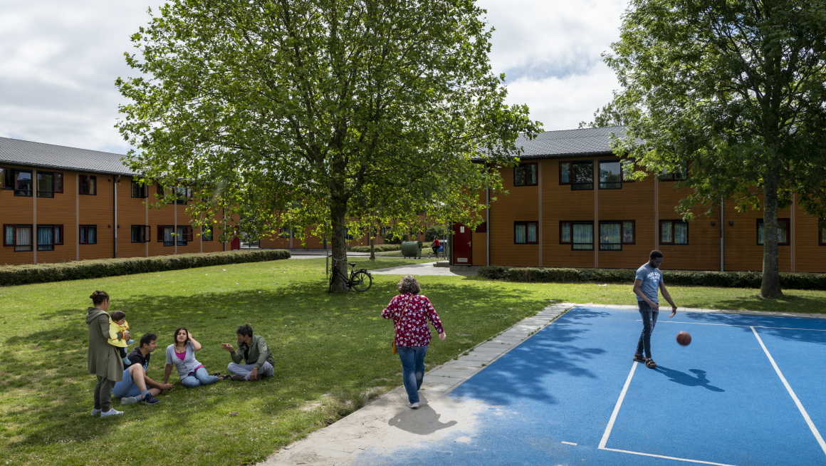 Gras met bomen met zittende bewoners en blauw sportveld met sportende bewoner