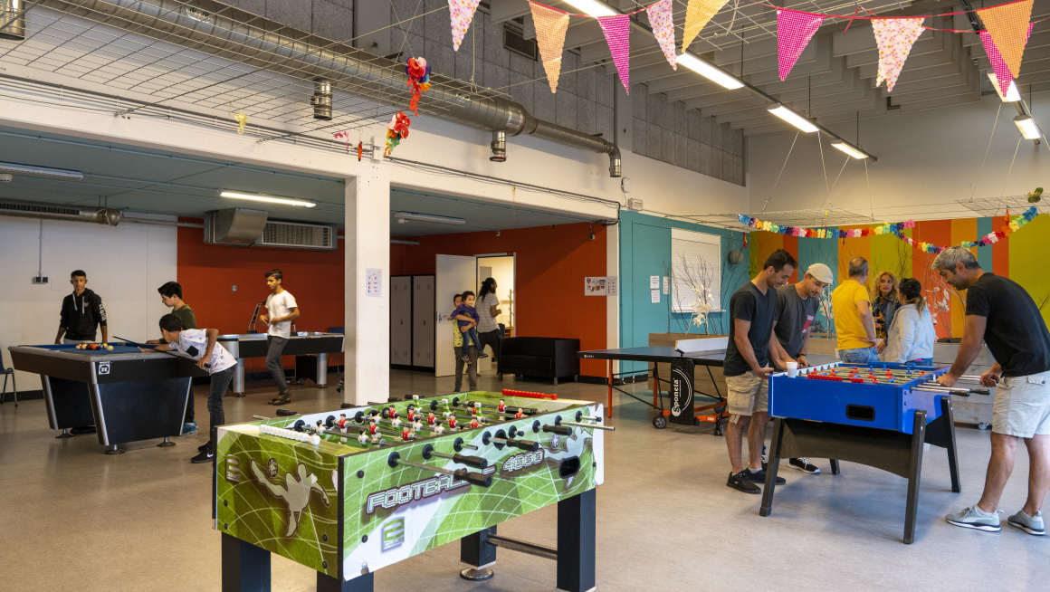 recreatieruimte met vrolijke vlaggetjes en bewoners actief met onder andere tafelvoetbal en biljart