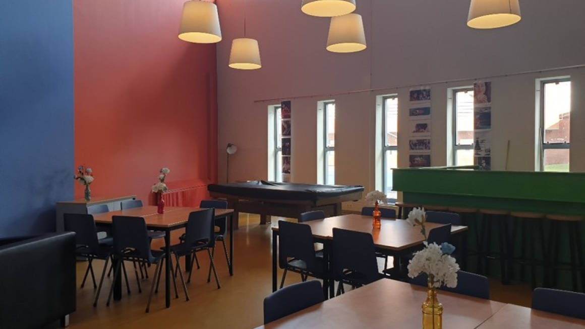 Recreatieruimte met blauw rode muur, tafels en stoelen en een bar