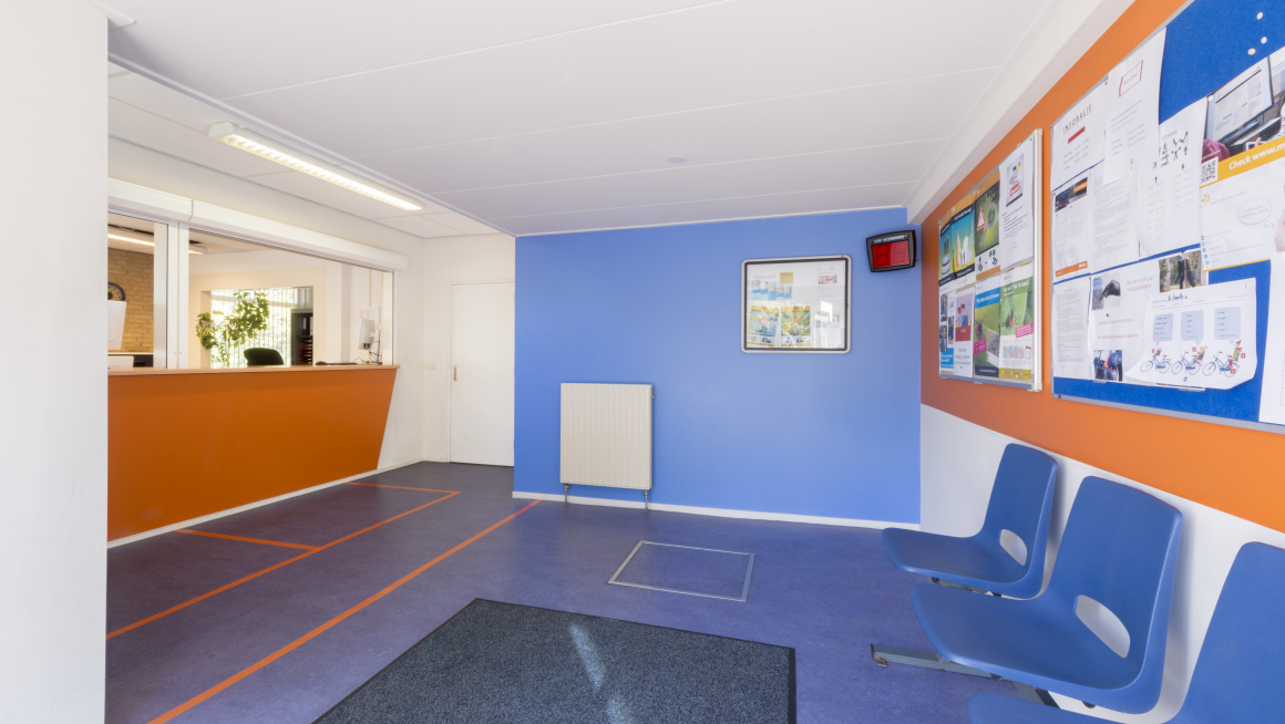 wachtruimte bij de informatiebalie met blauwe stoelen, blauwe vloer met mat en blauw, oranje en witte muren