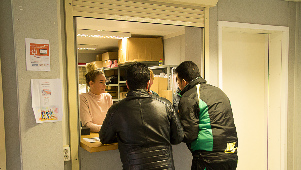 2 mannen bij een loket met daarachter twee medewerkers en stellingen met dozen