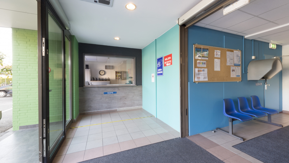 Ingang locatie met receptie, blauwe en groene muren en blauwe stoelen voor wachtenden