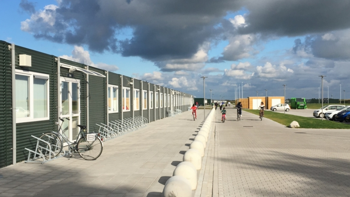 Groen gebouw met plat dak met fietsenrek en parkeerplaats ervoor