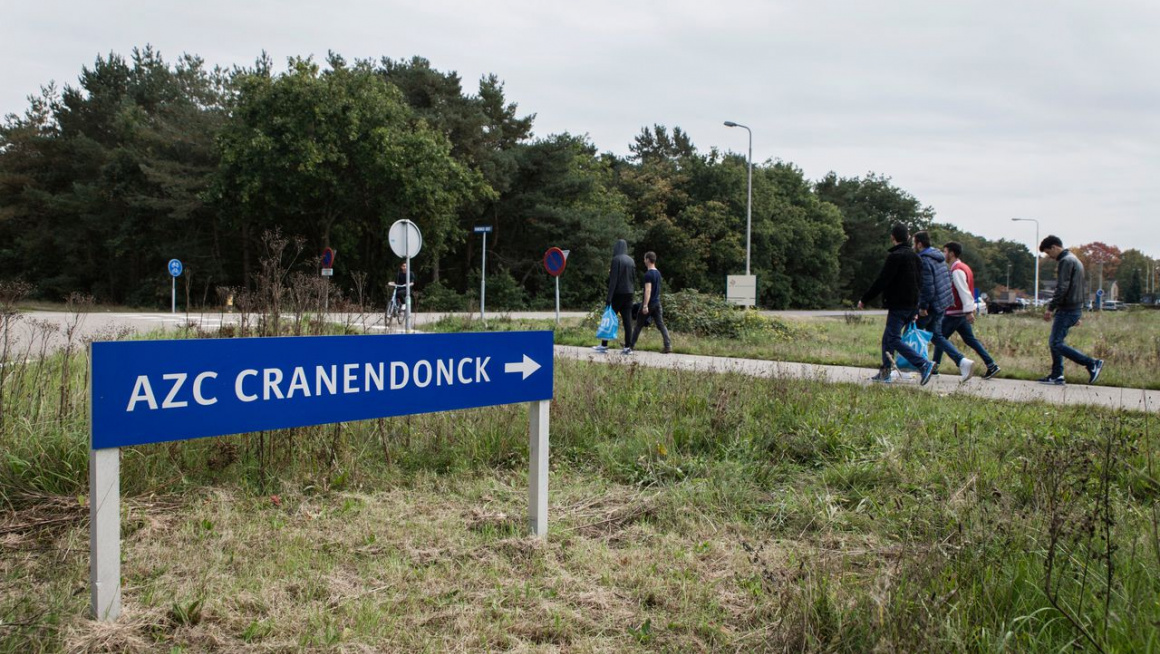 weg naar het azc met lopende bewoners en een verwijzingsbord