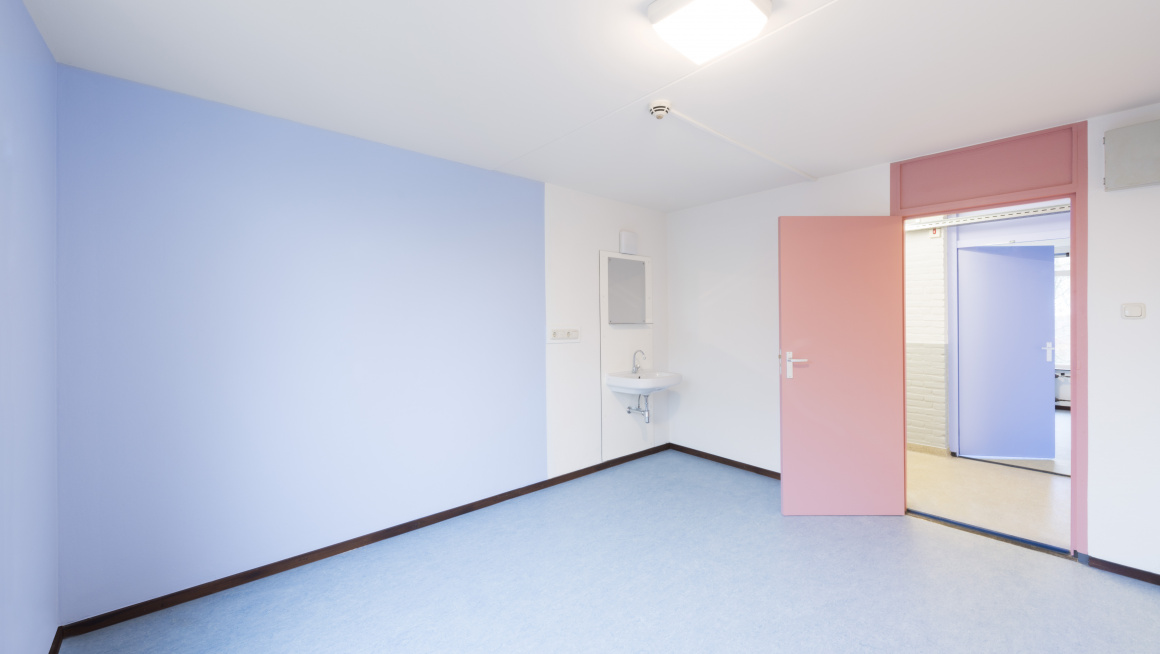 Lege bewonerskamer met blauwe muur en roze deur en een wastafel met spiegel
