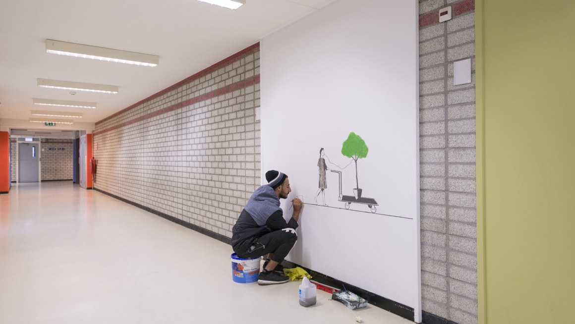 Bewoner in de gang zittend op een verfpot en bezig met een schildering op de muur van iemand die op een kar een boom verplaatst