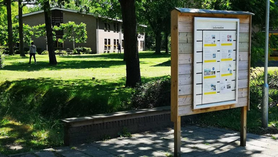 Informatiebord buiten met op de achtergrond gras en en gebouw