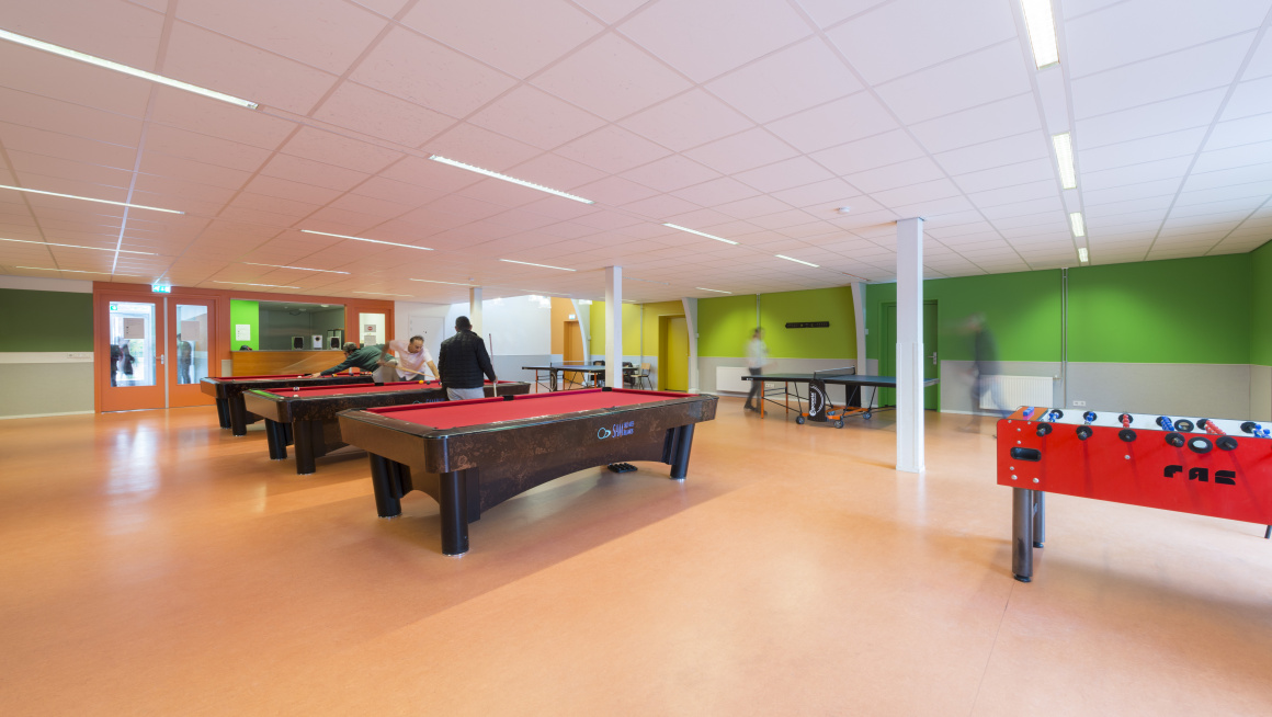 recreatieruimte met 3 pooltafels en een tafelvoetbal, licht oranje vloer en wit groene muren
