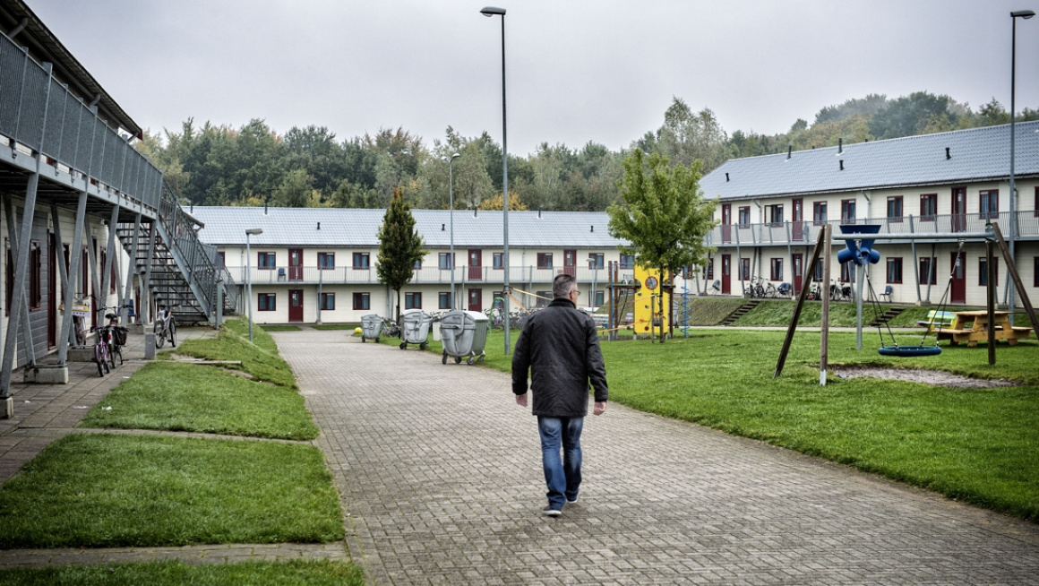 buitenterrein met gebouwen links, rechts en voor, daartussen gras en speeltuin en een pad waar een man loopt