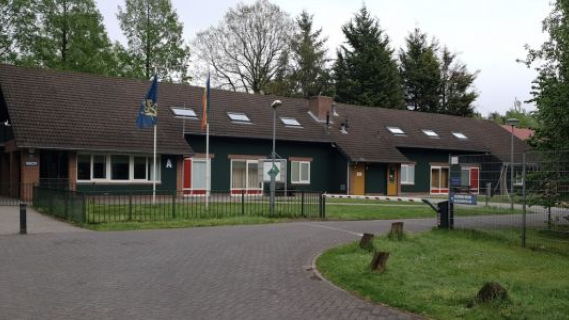 receptie, laag gebouw met slagboom en gras ervoor en bomen er omheen