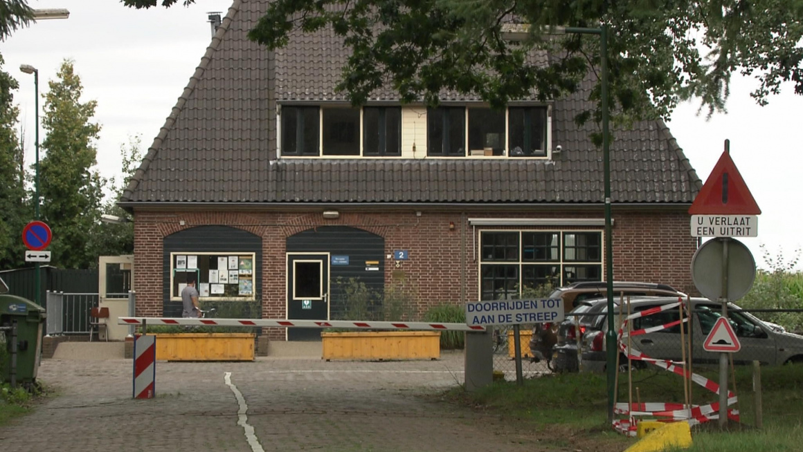 ingang azc met slagboom voor een gebouw met daarin de receptie