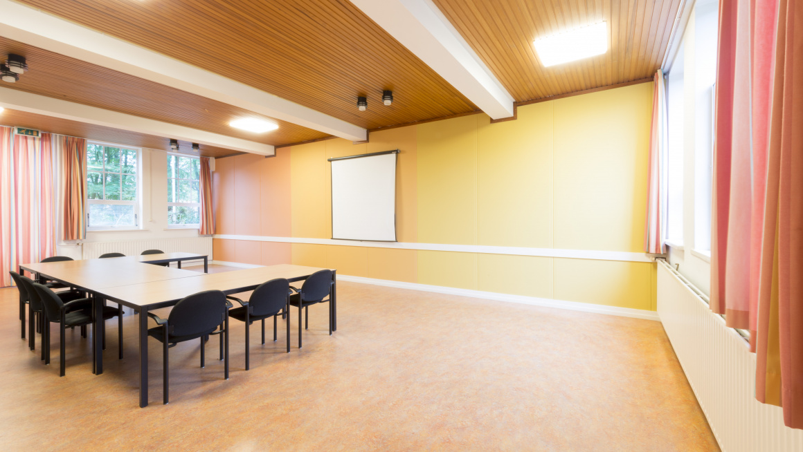 vergaderzaal met beige vloer en witte, oranje en gele muren, tafels en zwarte stoelen