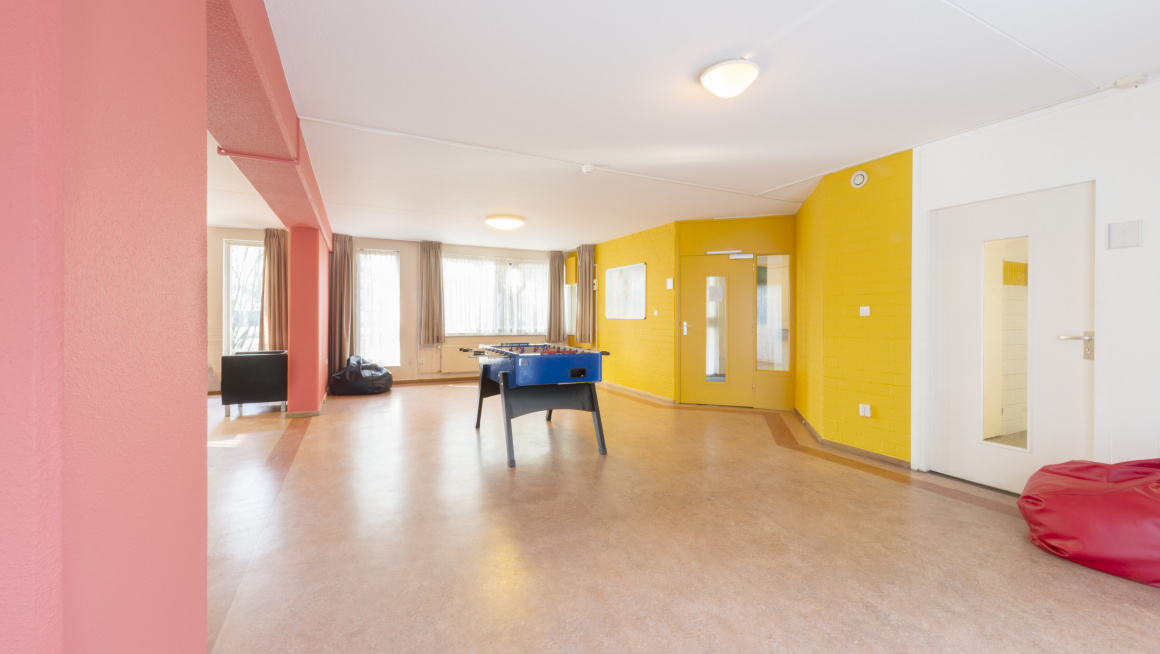woonkamer met beige vloer, roze, gele en witte muren, een zwarte en rode zitzak en een tafeltennistafeltafelvoetbal