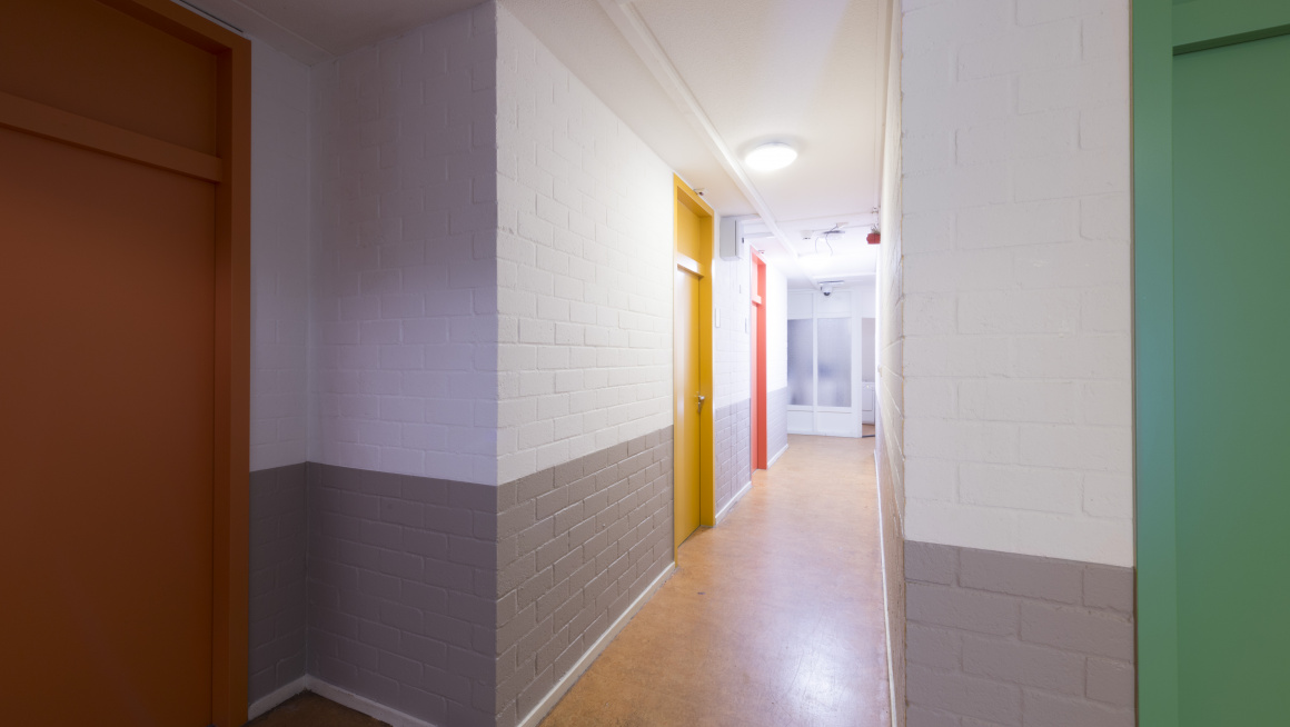 gang met een gele vloer, grijs/witte muren en deuren in geel oranje, rood en groen