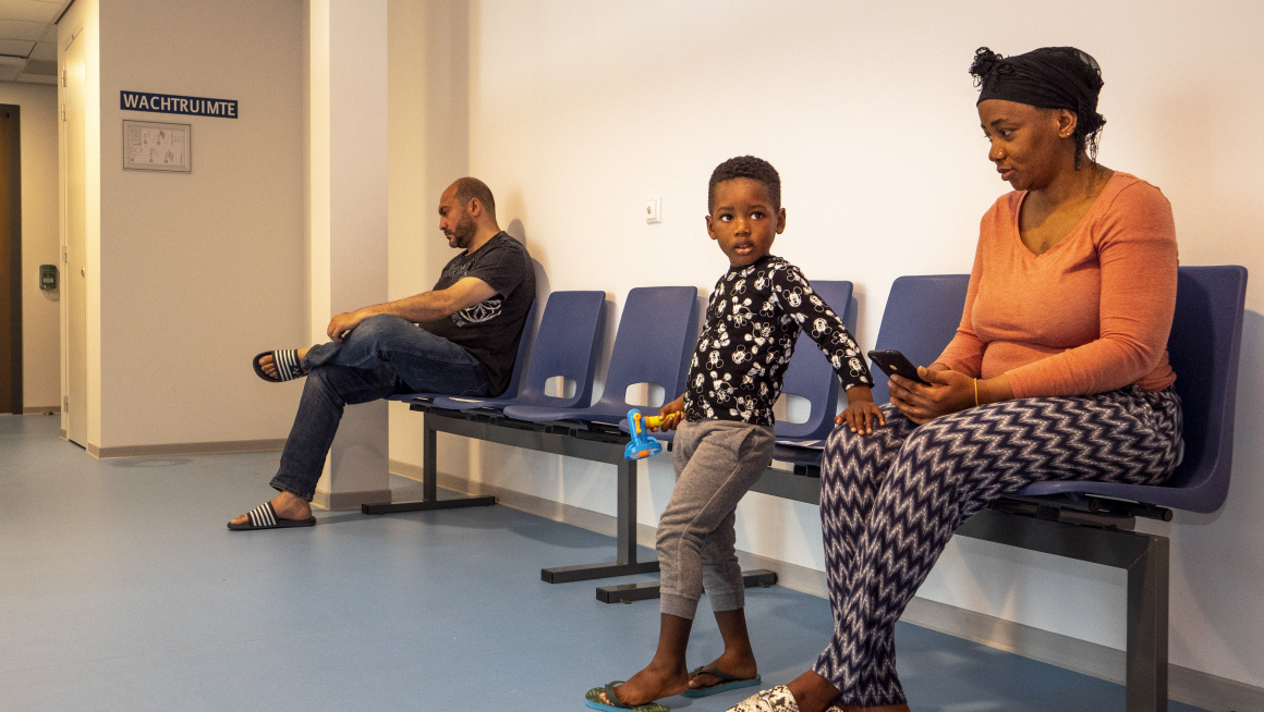 een man, vrouw en kind wachtend op blauwe stoelen bij de receptie