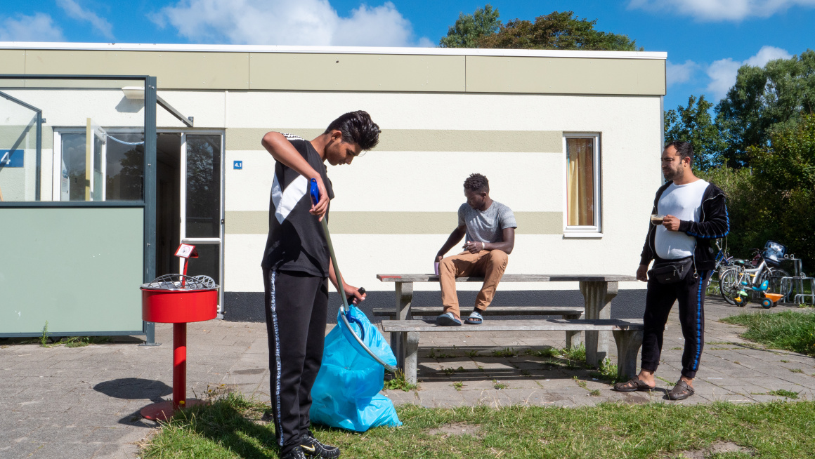 Bewoners die het terrein opruimen, zelfwerkzaamheid, voor een wit met beige gebouw