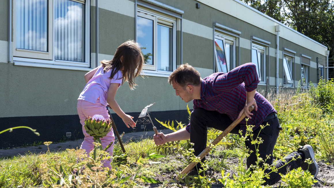 Man en kind werkend in de tuin voor een gebouw