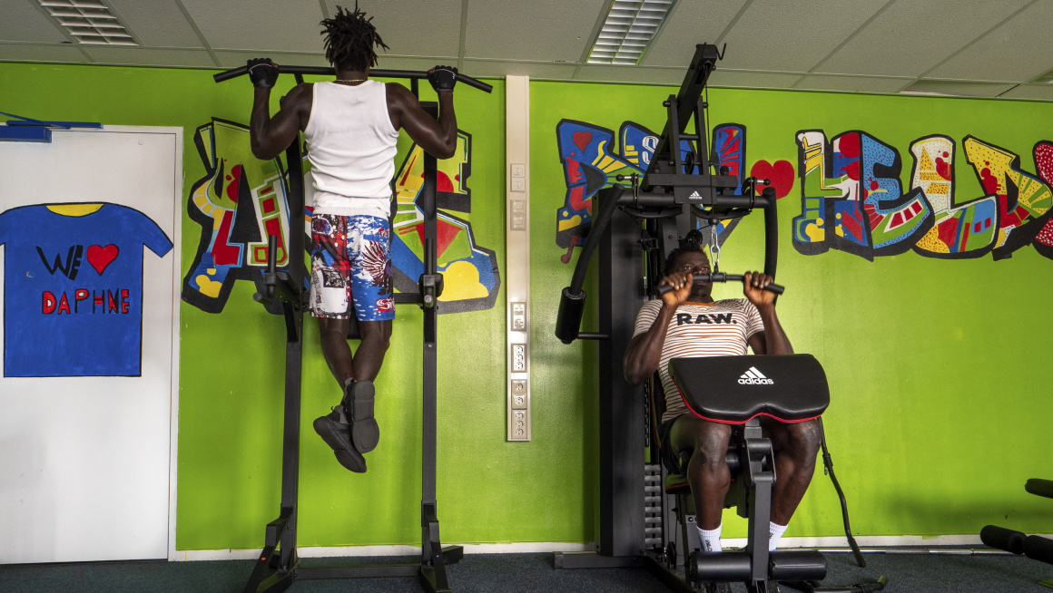 Twee bewoners op fitnessapparatuur voor een fel groene muur met grafitti